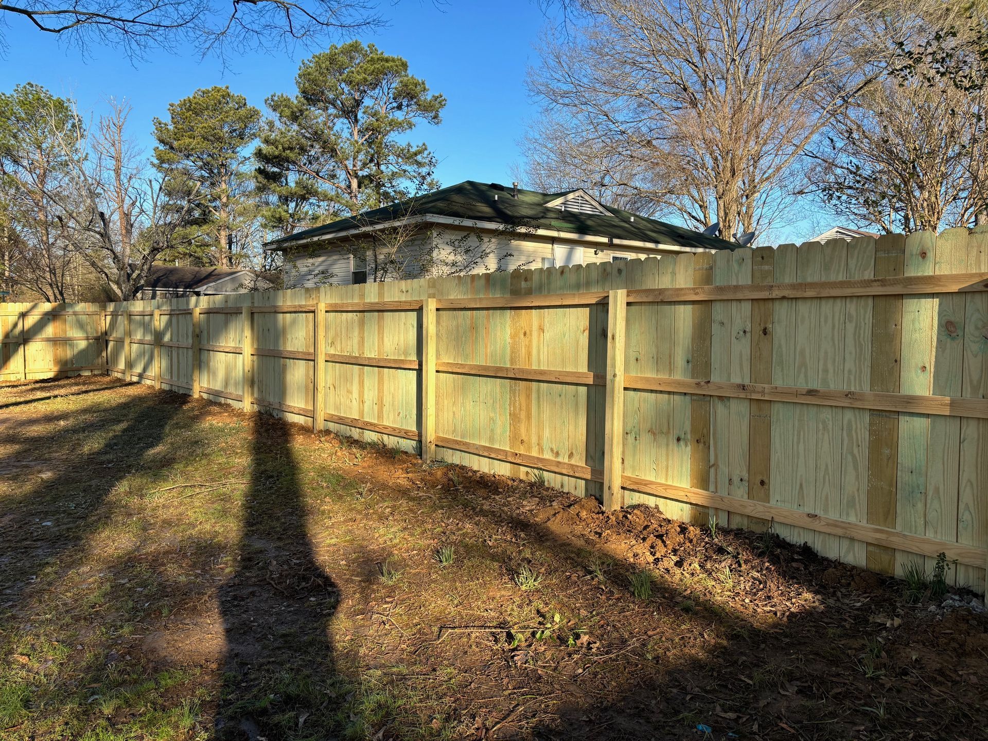 Wooden fence in a yard, casting a shadow on the ground.