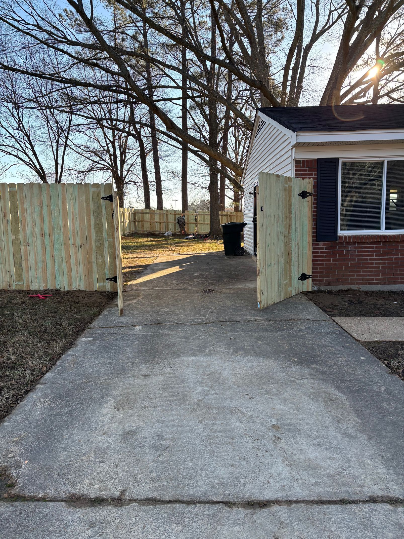 Concrete path leading to a gate in a wooden fence, beside a brick house.