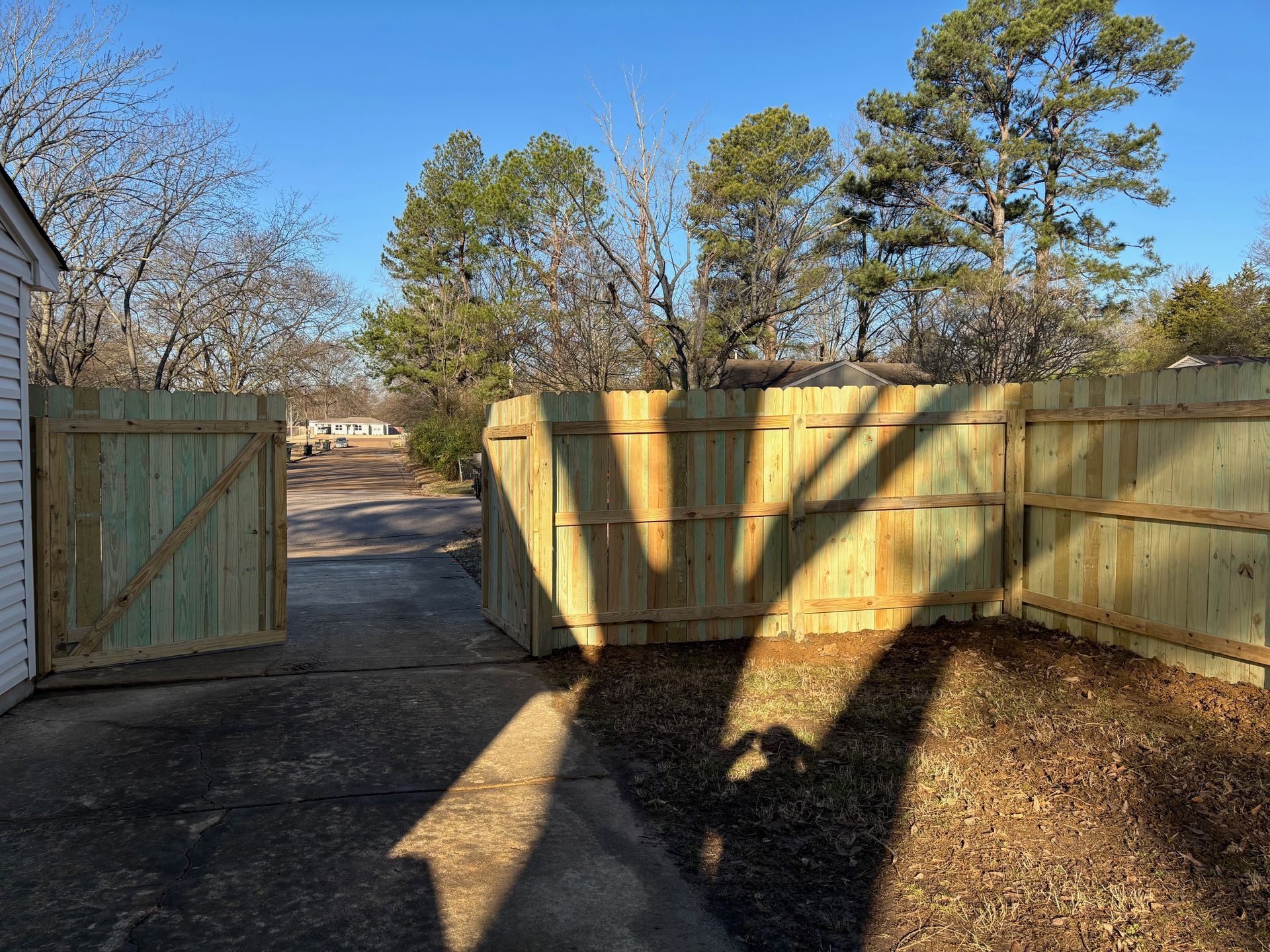 Wooden fence with gate open to a driveway, under a bright blue sky.