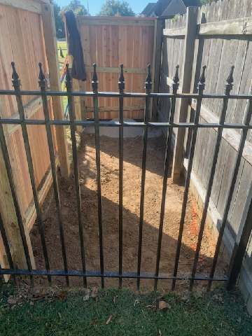 Black iron gate in a dirt yard, flanked by wooden fences.