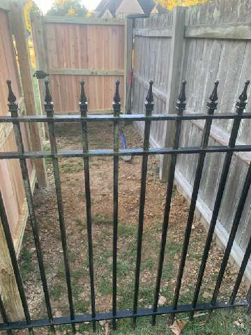 Black iron fence in front of a dirt patch between two wooden fences.