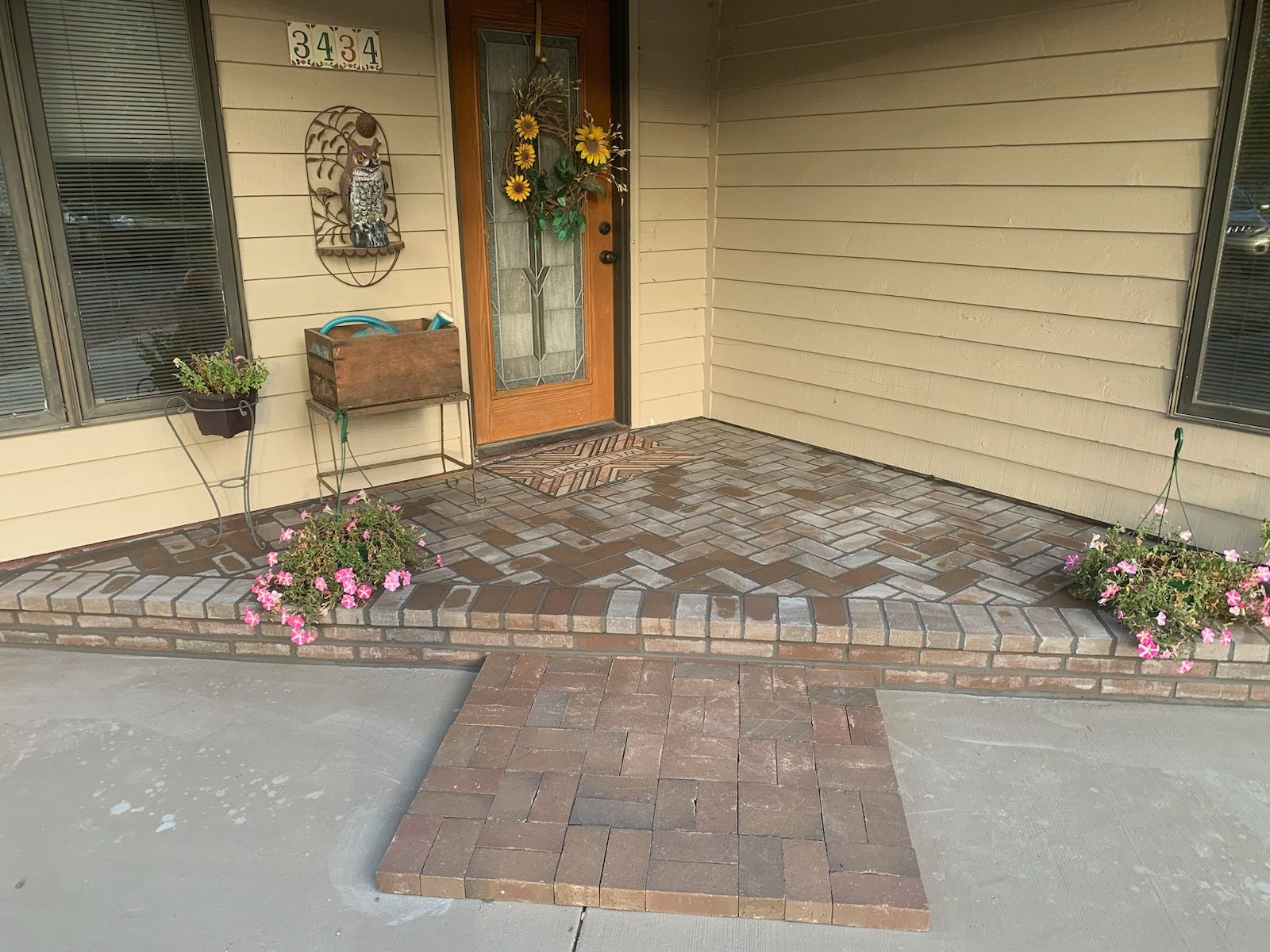 Brick entryway with a wheelchair ramp. Pink flowers on either side. Brown door with sunflower wreath.