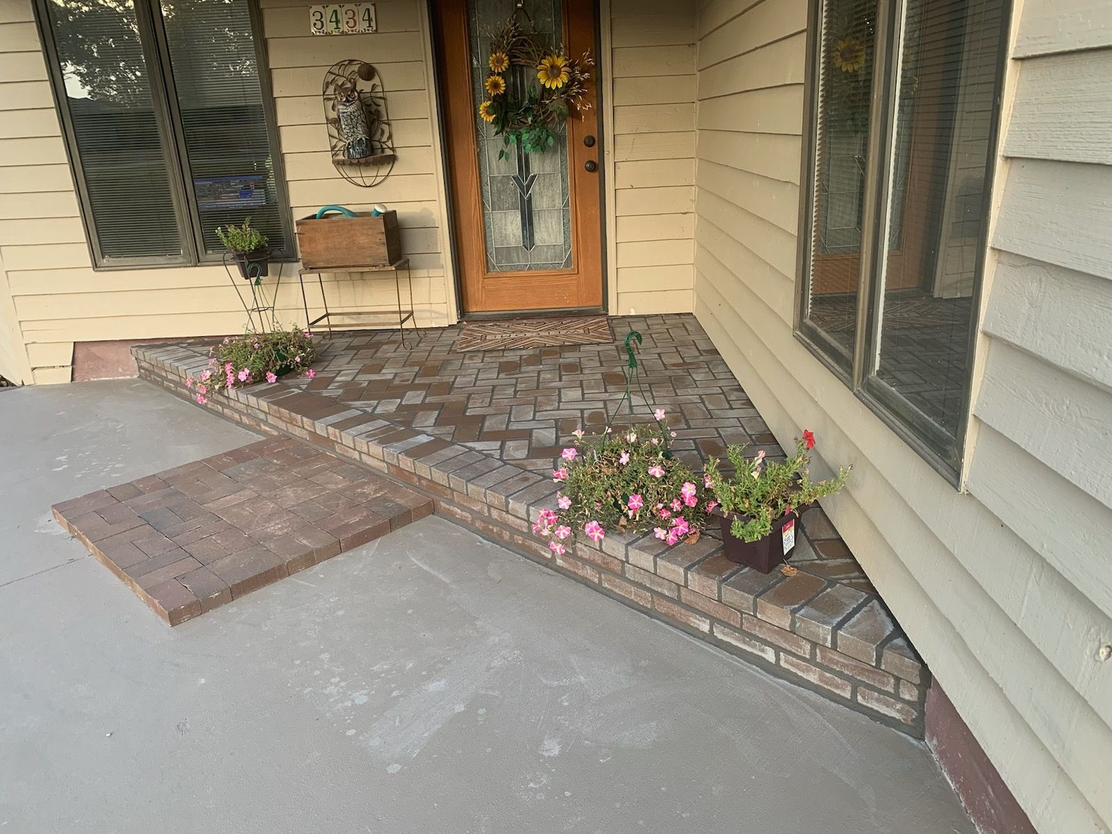 A front porch with brickwork, flowers, and a brown door; the house has beige siding.