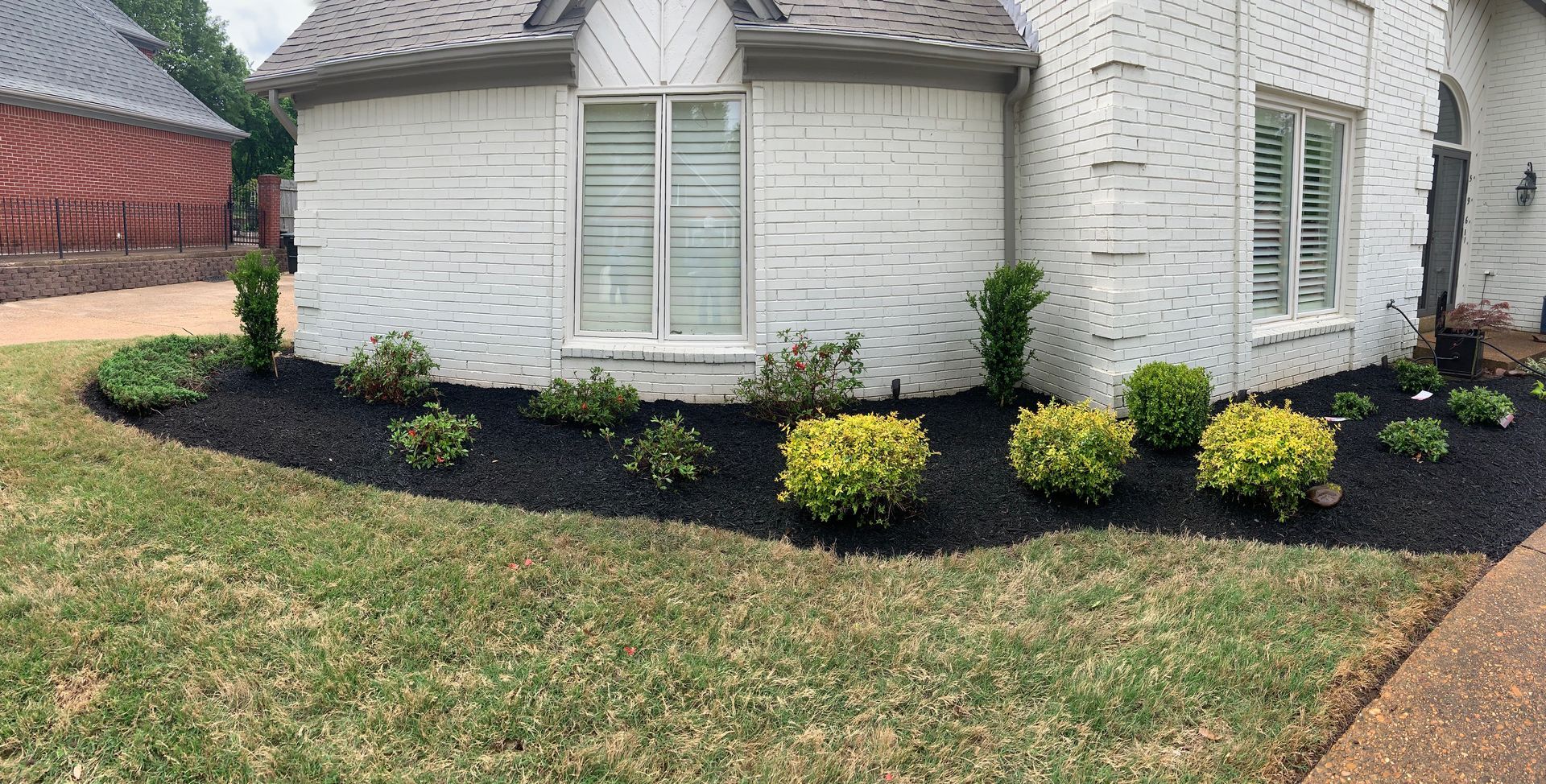 A house with a brick facade and manicured landscaping, including black mulch and trimmed shrubs.