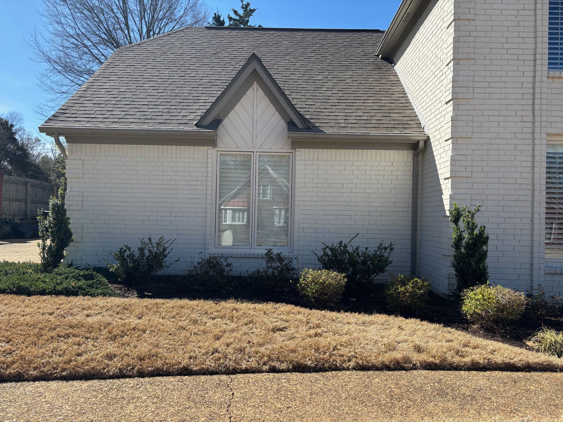 White brick house with a gray roof, brown grass, and a clear blue sky.