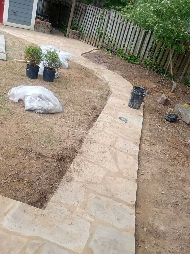 Stone pathway winding through a yard, bordered by grass and a fence.