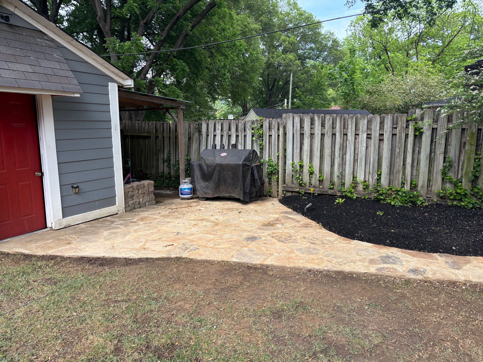 Backyard with grill under a cover, gravel patio, wooden fence, and shed with a red door.