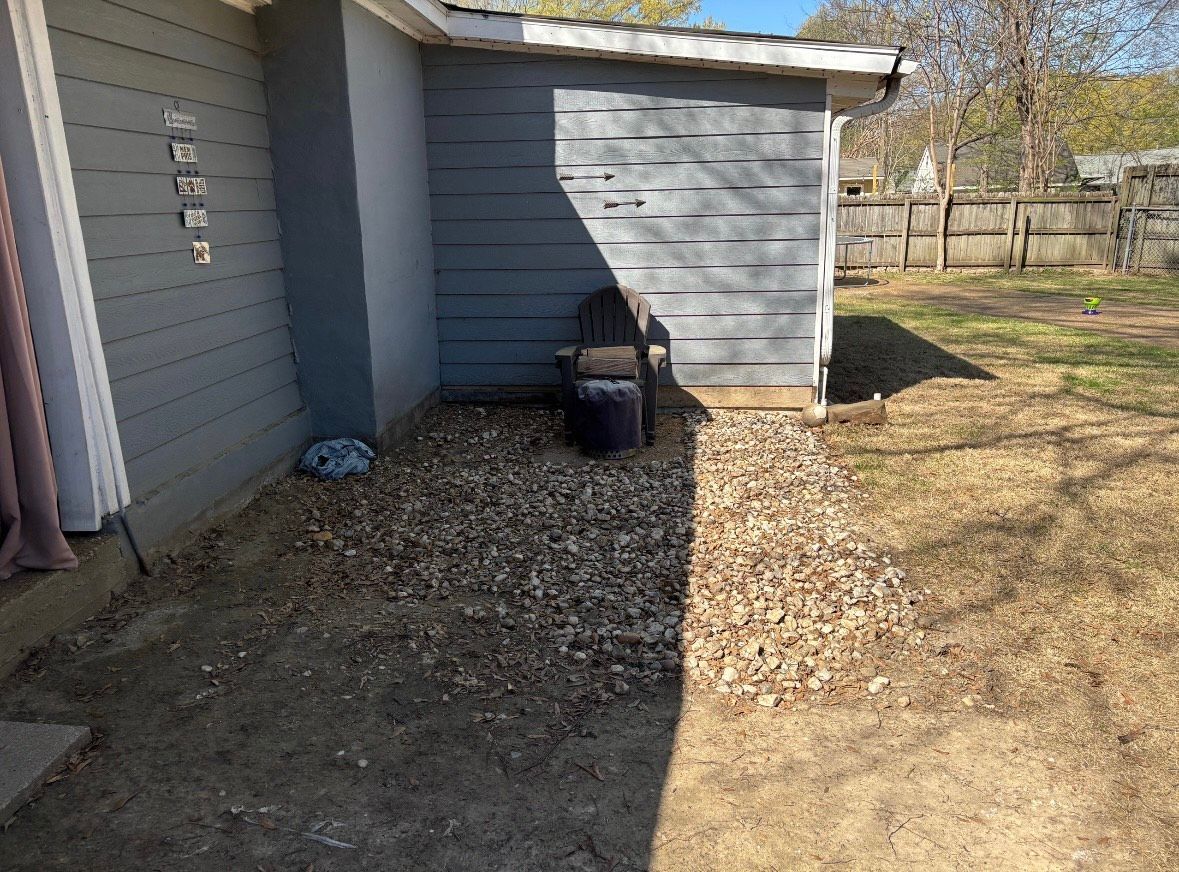 Backyard with a gravel area next to a gray shed and siding. A chair sits in the gravel.