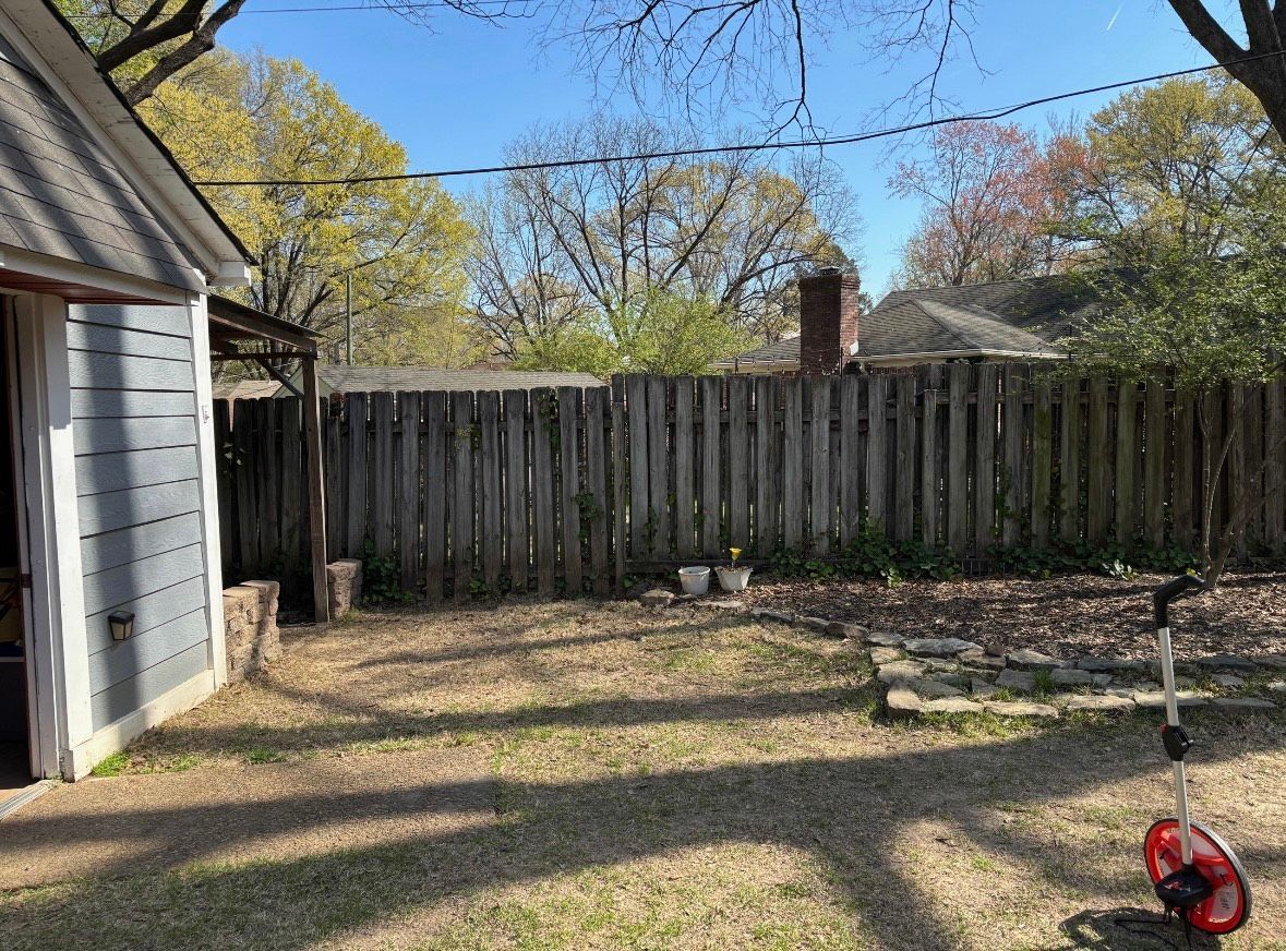 Backyard with wooden fence, shed, green grass, and trees on a sunny day.