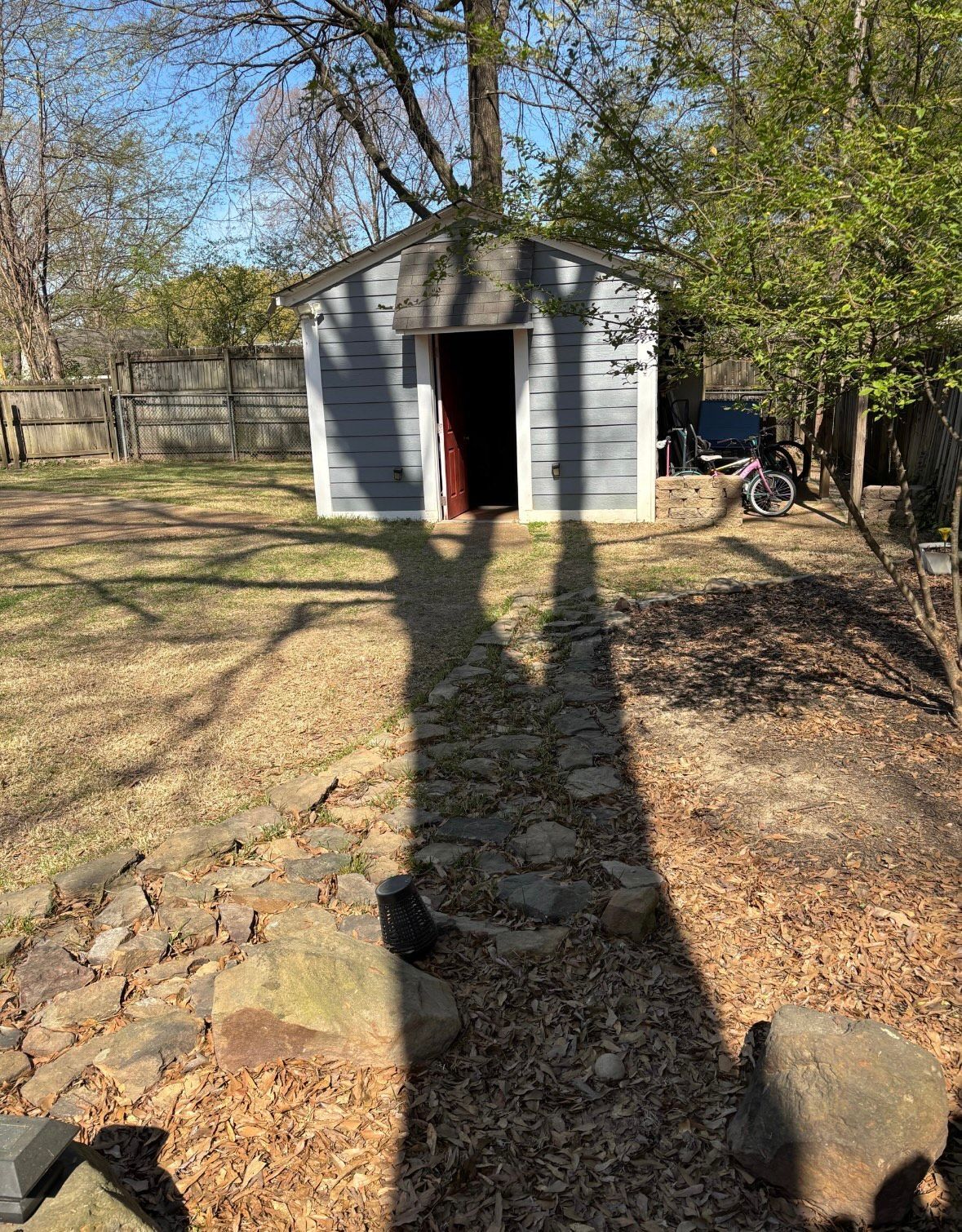 Shed in a backyard; long shadow of a person or object cast on the ground.