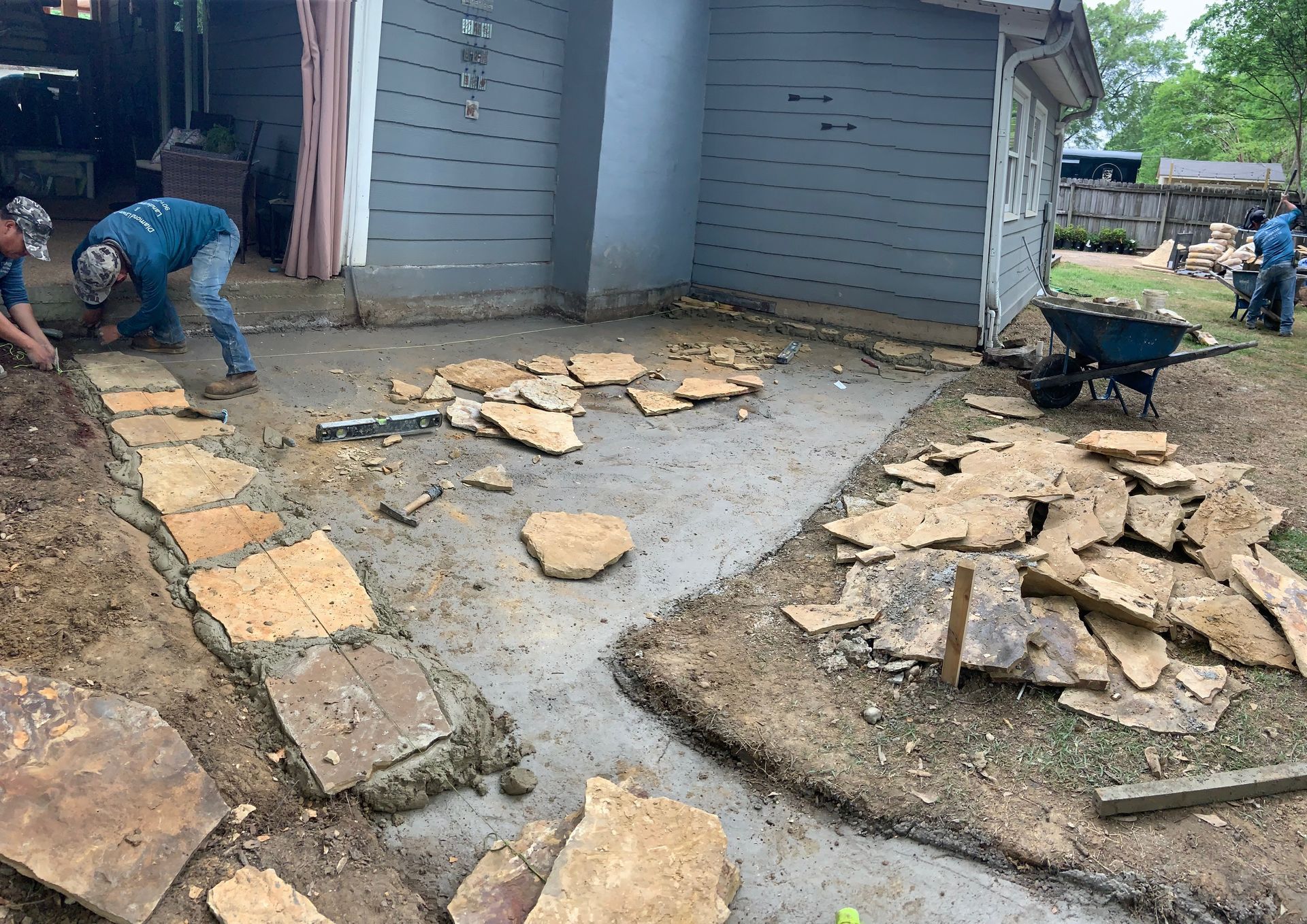 Workers installing stone pavers on a concrete patio.