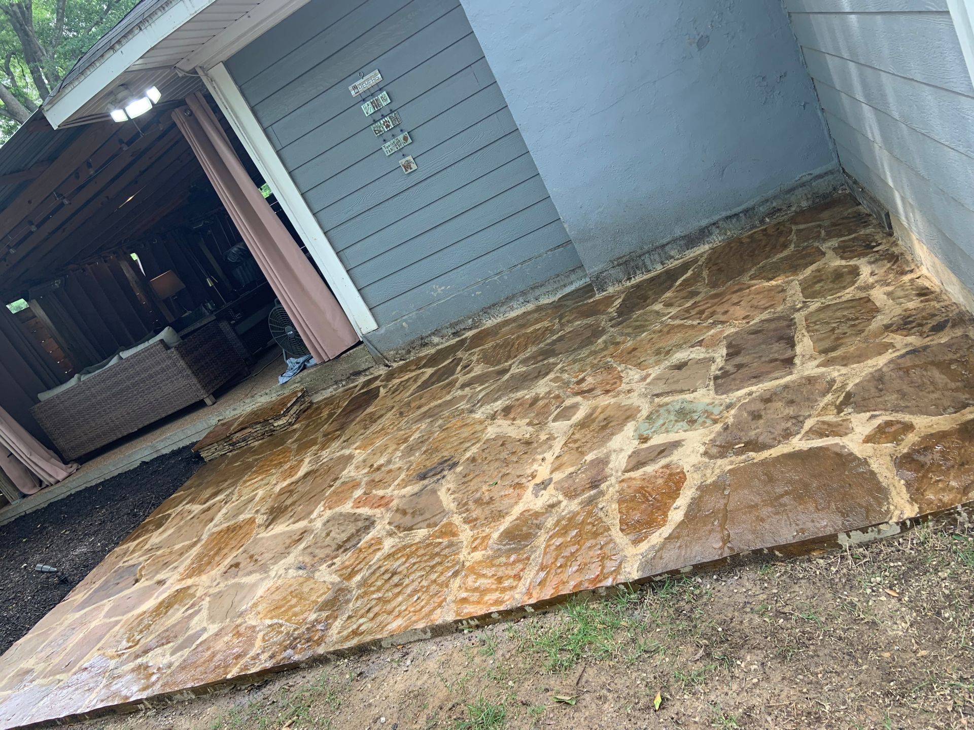 Stone patio, wet from rain, against a light blue house with a covered porch.