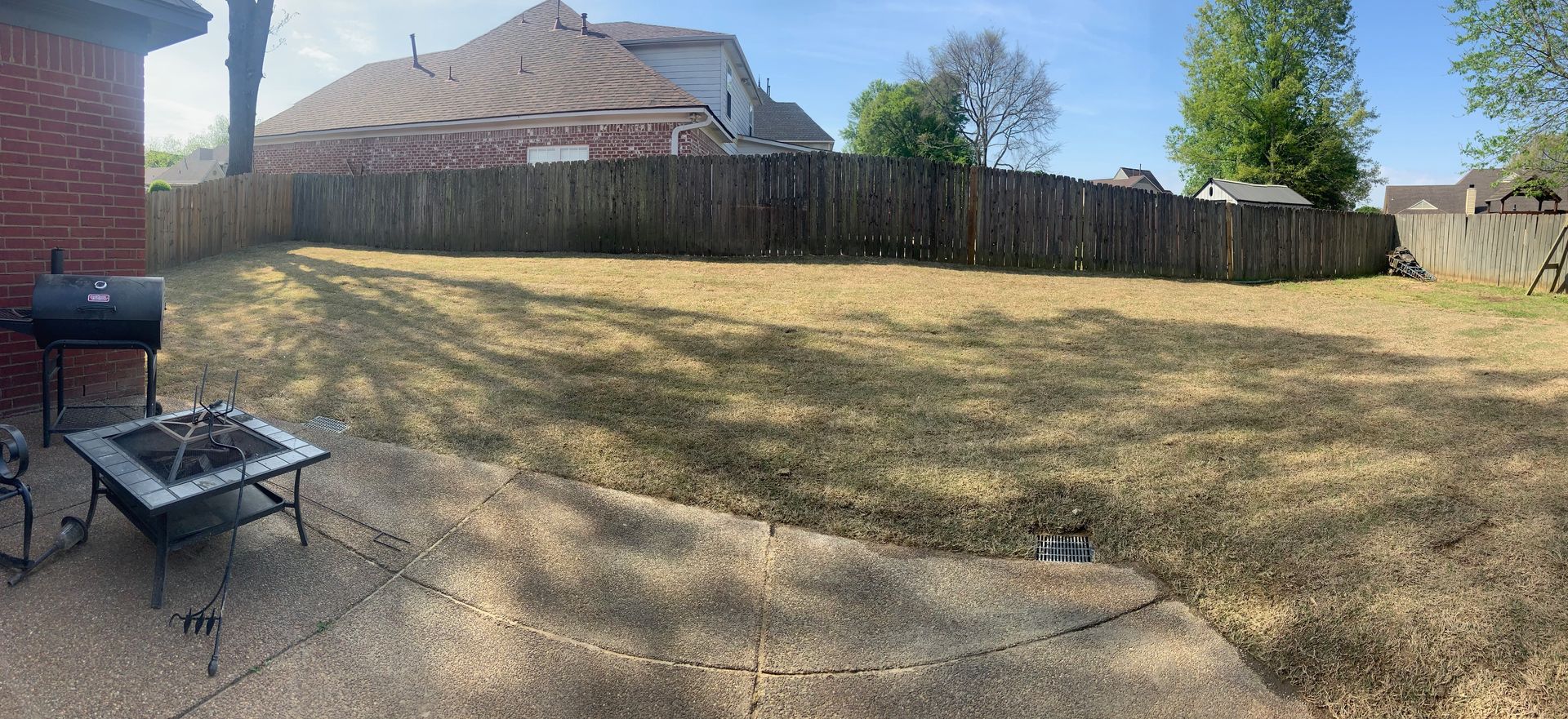 Backyard with a fire pit, grill, and a wooden fence surrounding dry grass.