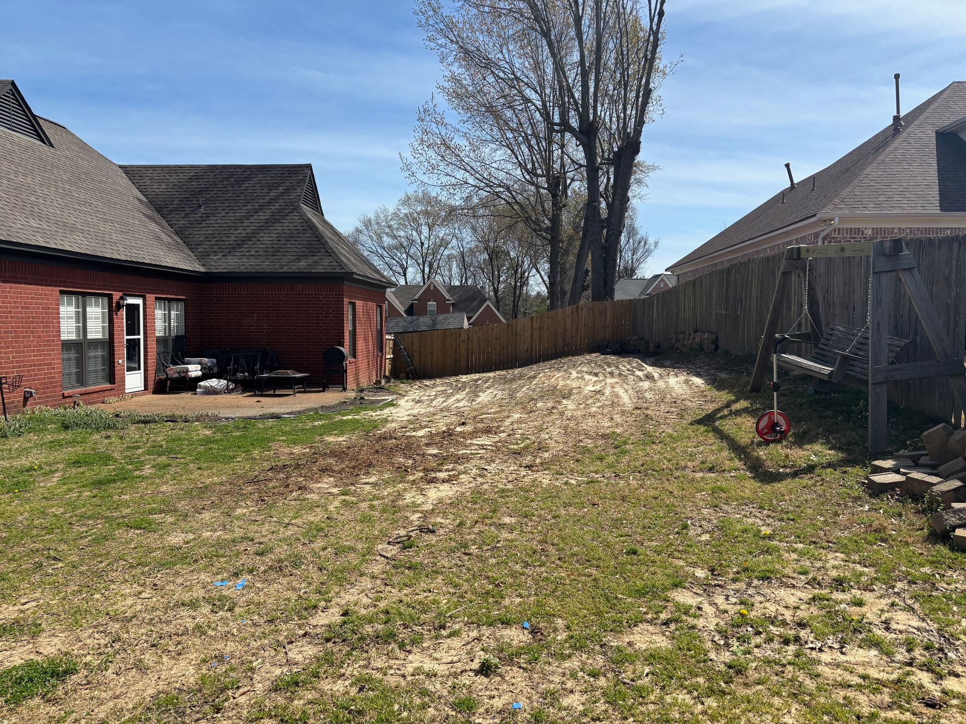 Backyard with dirt pile between two brick houses and wooden fence under blue sky.