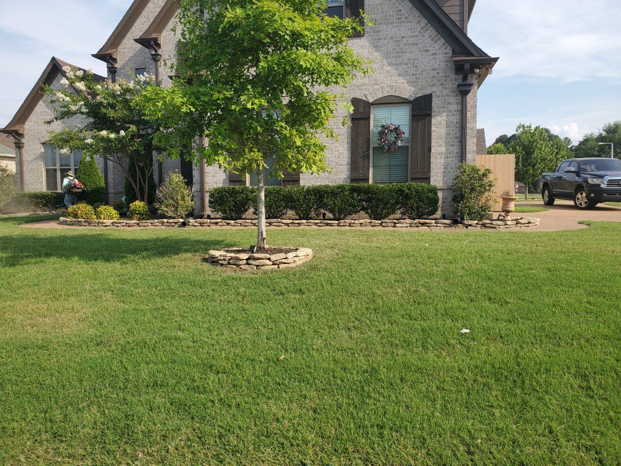 House with manicured lawn, landscaping, and a parked truck on a sunny day.