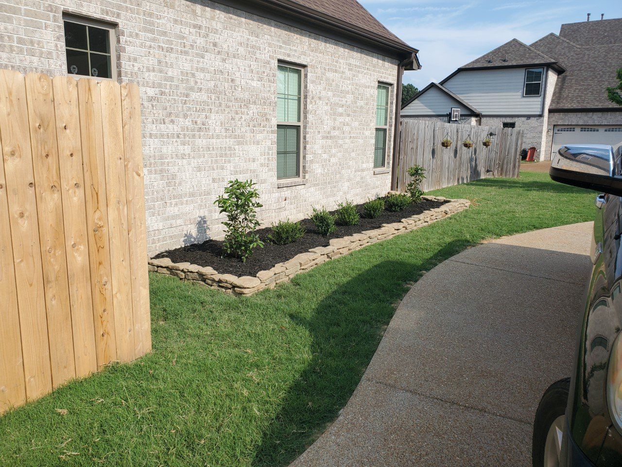 A brick house with a garden bed, green grass, a wooden fence, and a curved driveway.