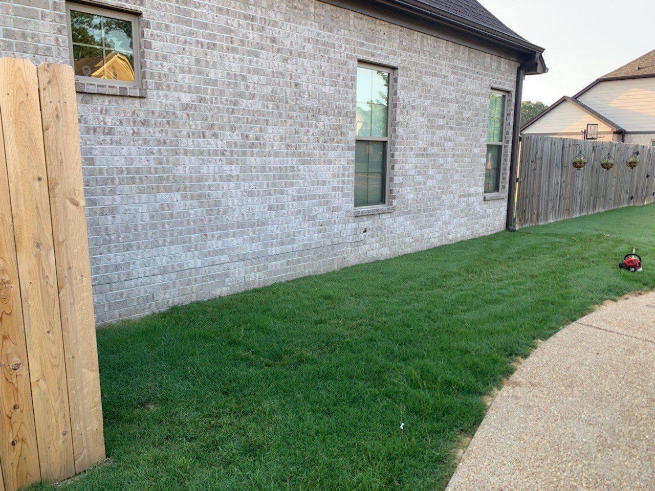 Green lawn along a brick house with windows and a wooden fence.