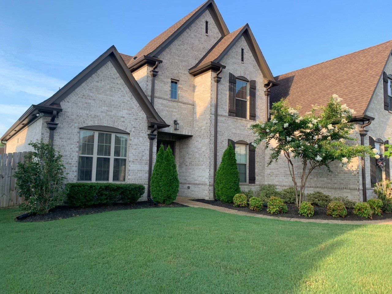 Two-story brick house with dark trim, green lawn, and small trees.