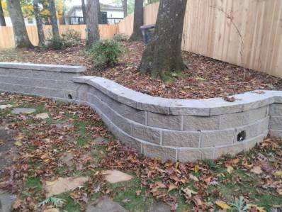 Stone retaining wall curves around a tree, with leaves scattered around.