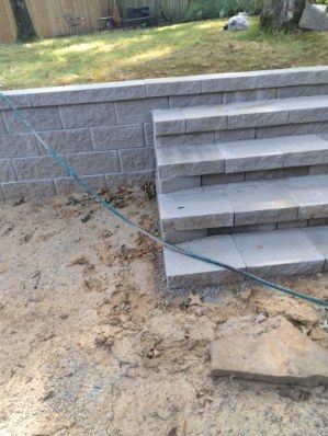 Stone retaining wall with steps leading up to grass. Sand and dirt in the foreground.