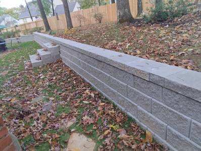 Stone retaining wall with steps on a grassy slope covered in fall leaves.