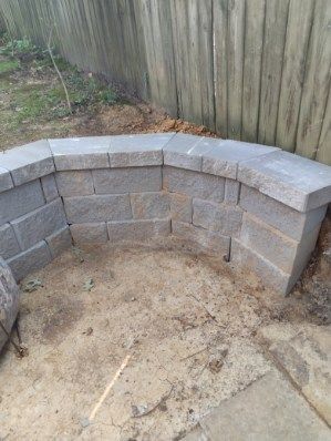 Gray block retaining wall in a yard, curving in front of a wooden fence.