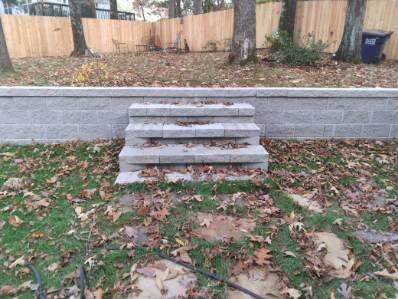 Stone steps leading up a small retaining wall covered in fallen leaves.