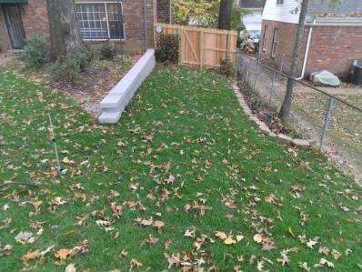 Green lawn with fallen leaves, concrete blocks, wooden fence, and a chain-link fence.