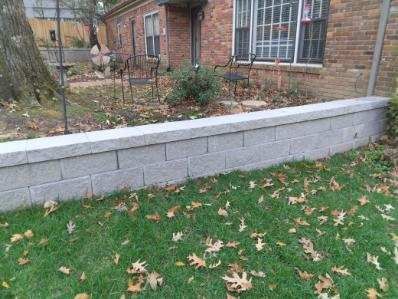 Gray retaining wall in front of a brick house with grass and fallen leaves.