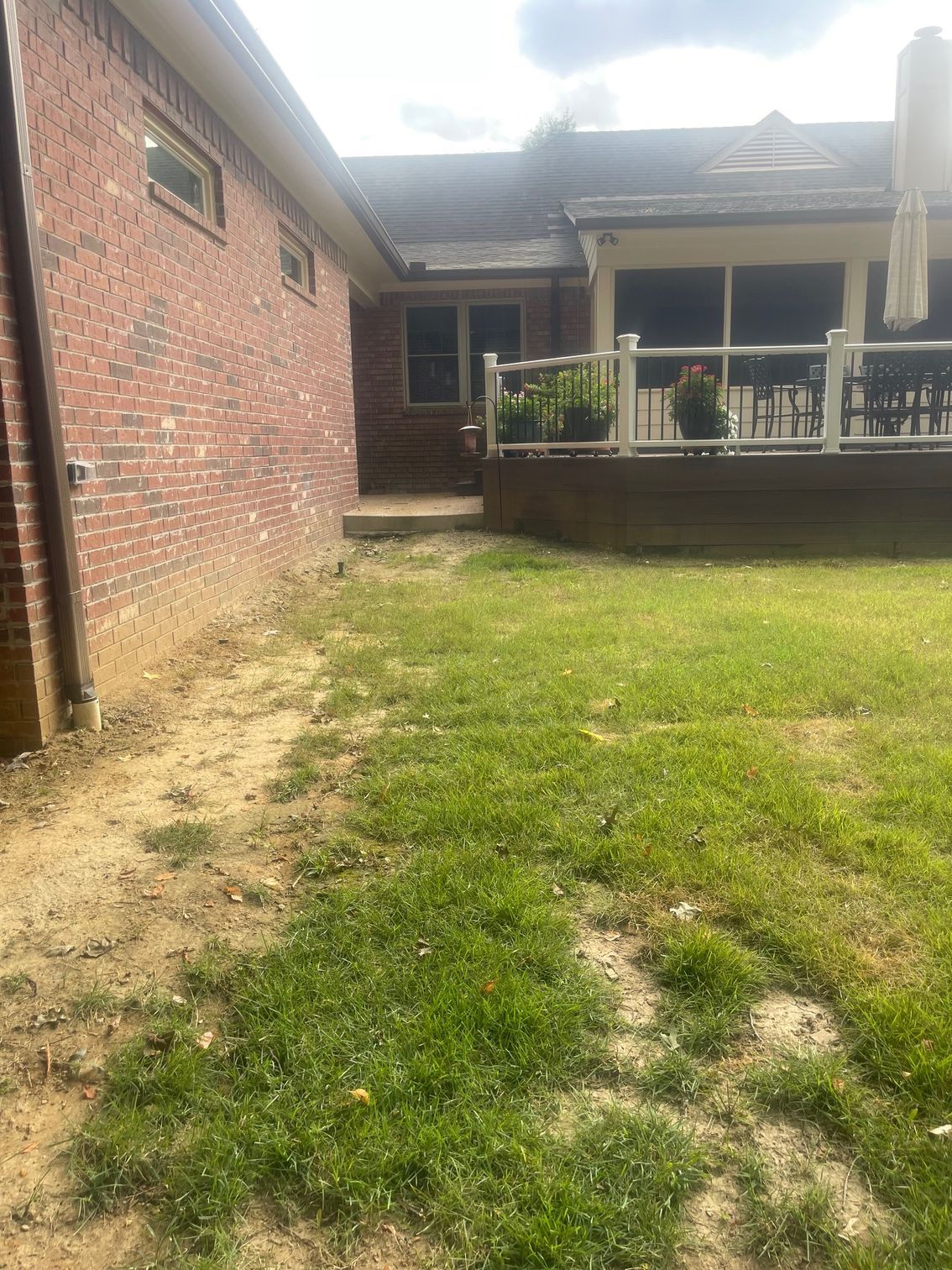 Brick house exterior with a patchy lawn leading to a wooden deck with a white railing.