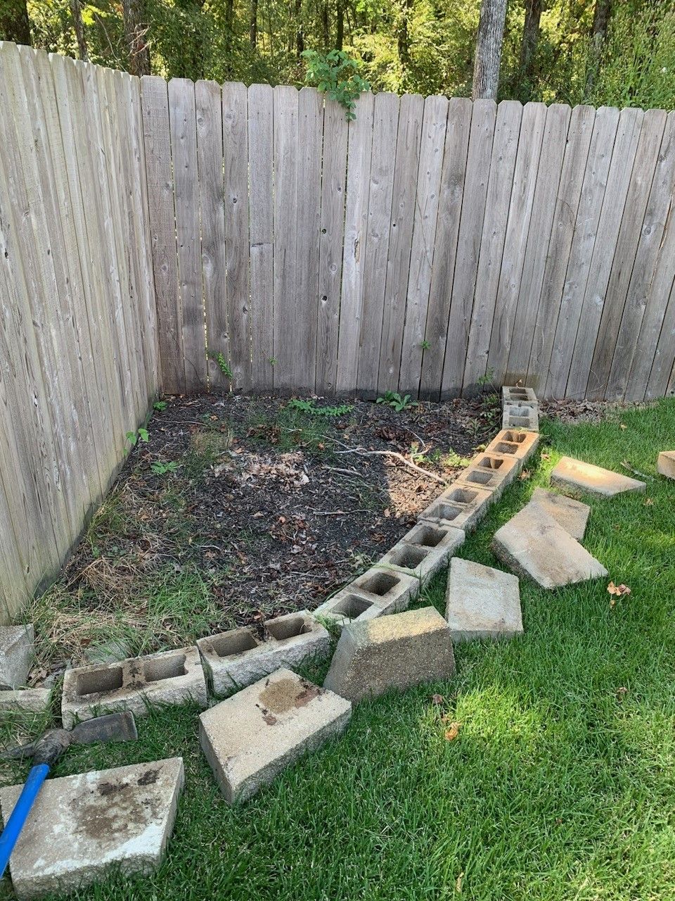 A small garden area with a wooden fence, cinder blocks, and grass.