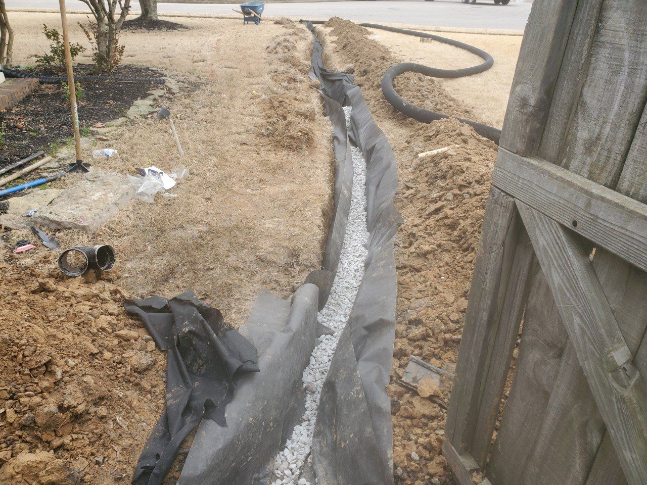 A trench with gravel and black fabric being installed in a yard for drainage.