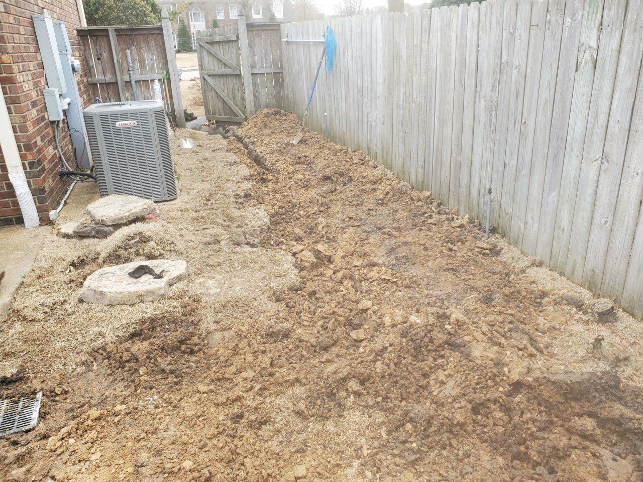Backyard with dirt, fence, air conditioning unit, and brick wall.