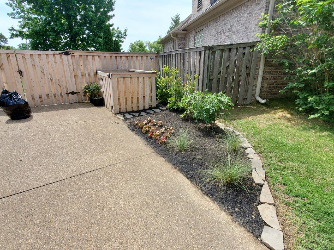 A backyard patio with a wooden fence, flower bed, and air conditioning unit.