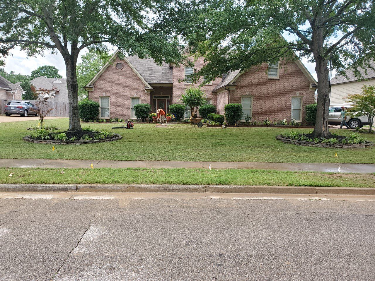 A brick house with trees in the front yard. A lawn is in front of the house.