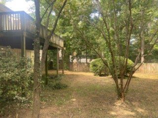 Backyard view with a wooden deck, trees, and a grassy area.
