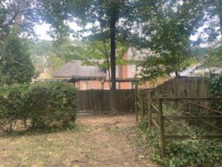 Backyard with fence, trees, and a building in the background.