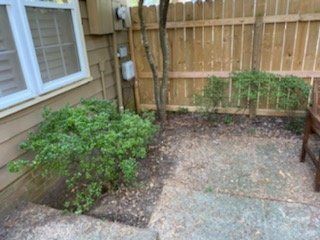 Small backyard with a wooden fence, paved patio, and bushes.