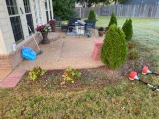 Backyard patio with brick trim, plants, tools, and lawn.