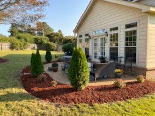 Backyard patio with seating, evergreen trees, and red mulch.