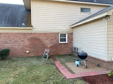 Backyard with brick patio, grill, and ladder next to a house with beige siding and brick walls.