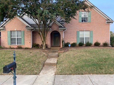 Brick house with green shutters and a walkway. A mailbox stands in the foreground.