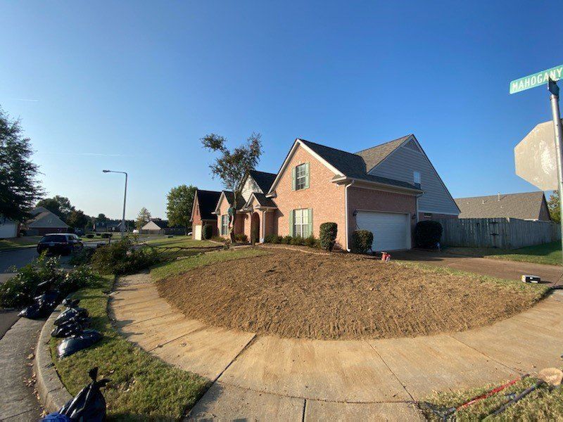 A brick house with exposed dirt lawn, sidewalk in the foreground, blue sky.