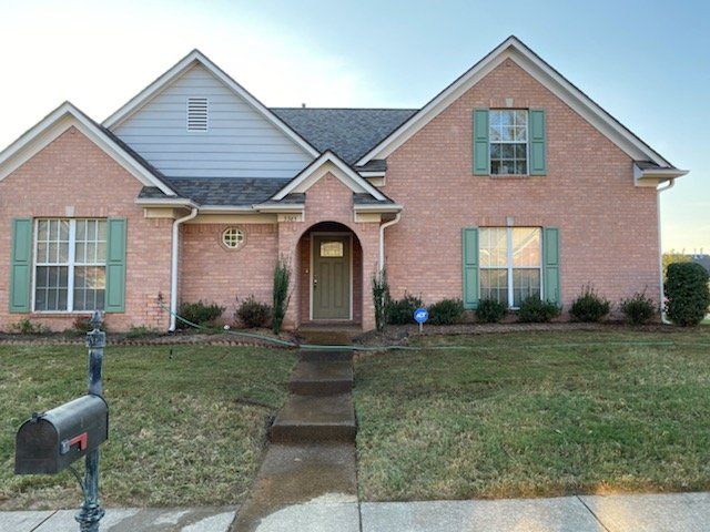 Pink brick house with green shutters and door, mailbox in front.