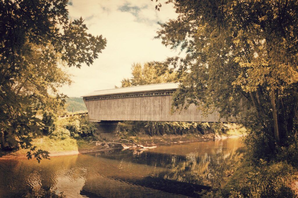a covered bridge over a river surrounded by trees in Vermont. Gorham Covered Bridge Circa 1842
