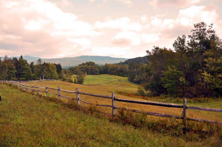 a wooden fence surrounds a grassy field with mountains in the background in Huntington, VT