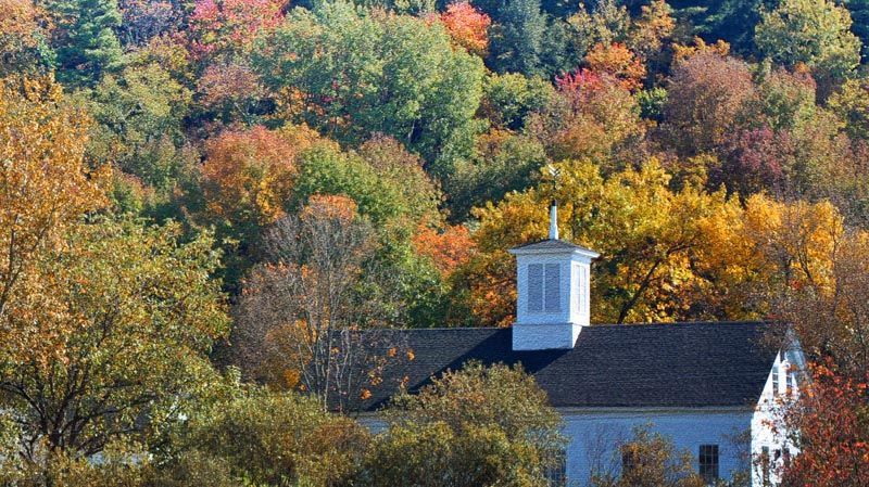 a white church is surrounded by trees with autumn leaves in Stowe, VT