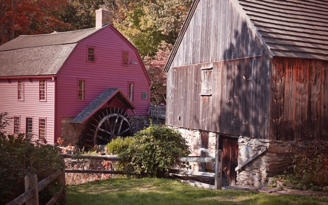 a pink barn and a wooden barn with a water wheel in the background .