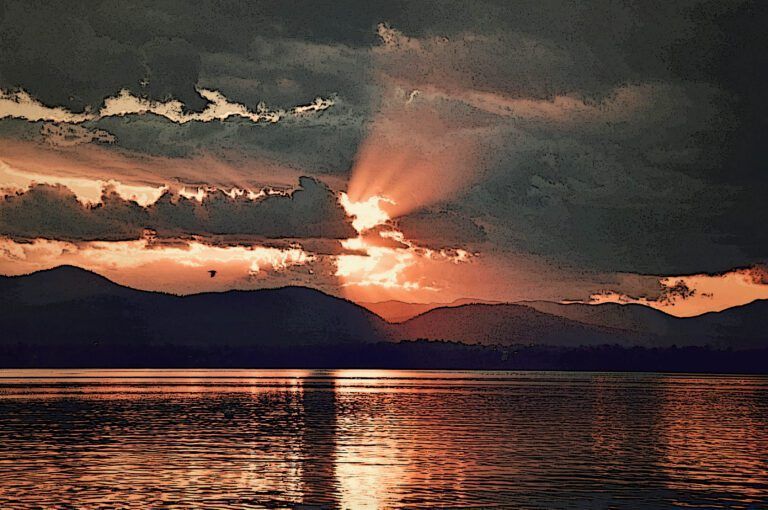 a sunset over a lake with mountains in the background