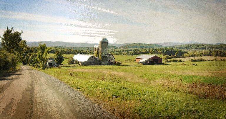 a dirt road leading to a farm with a silo and a barn, The Champlain Valley